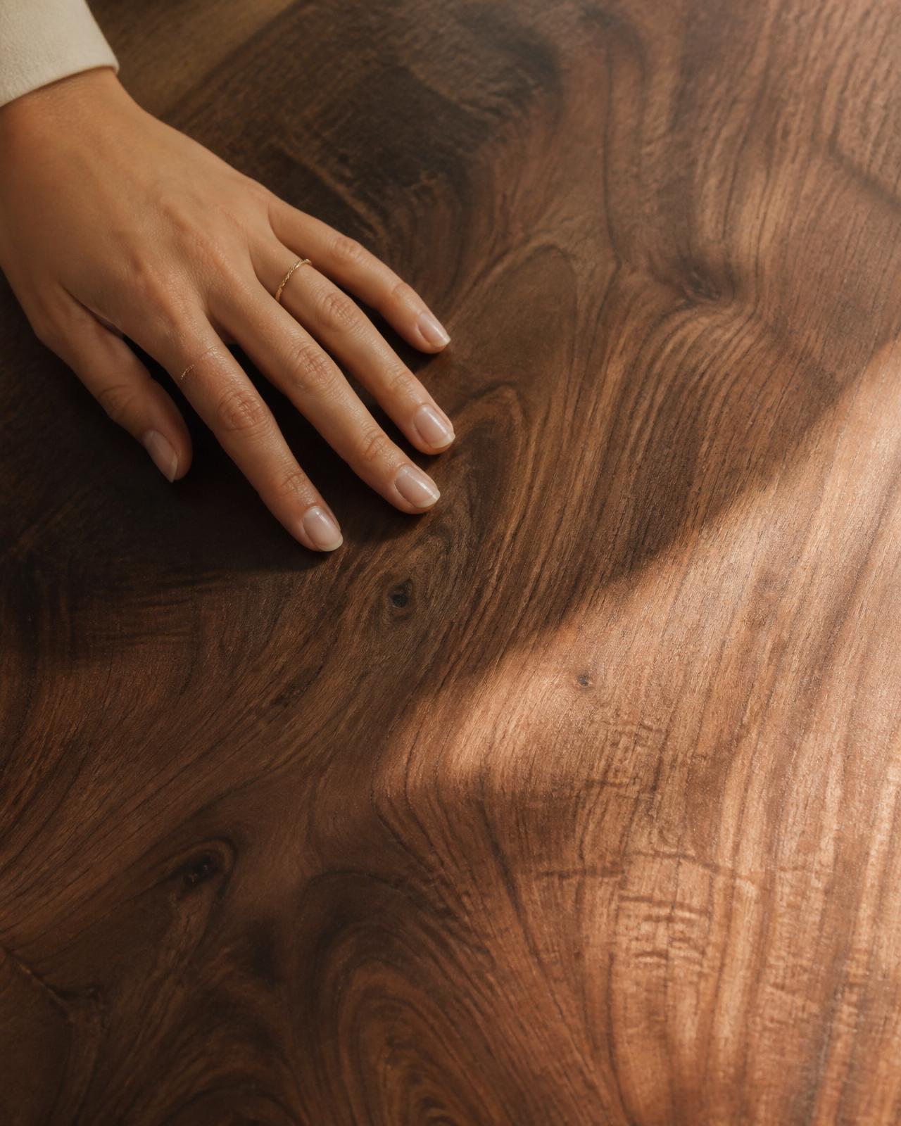 A hand resting on the grain of a solid walnut tabletop